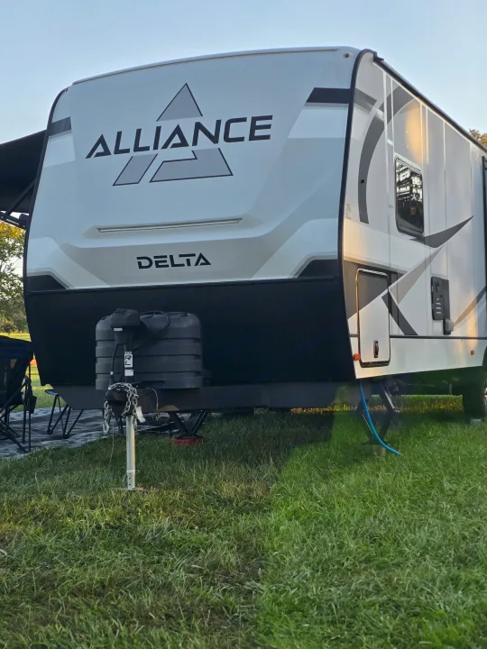 Alliance Delta RV rental: a white & black travel trailer parked on green grass, setup for camping with propane tanks visible.. Alliance Delta 292RL 2025
