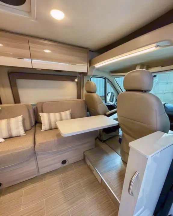 Interior view of an rv rental, showcasing the convertible dinette area with cushioned benches, overhead cabinets, and front swivel seats.. Thor Sequence 2022