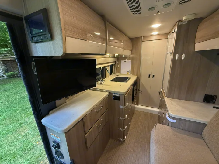Modern RV rental interior with a kitchenette, sink, stove, TV, and light wood cabinets, plus a cozy seating area.. Thor Sequence 2022
