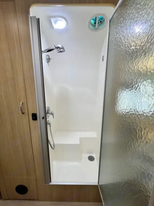 Clean, compact shower stall in an RV rental, featuring a built-in step, handheld shower, vent, and textured door.. Airstream Flying Cloud 2018