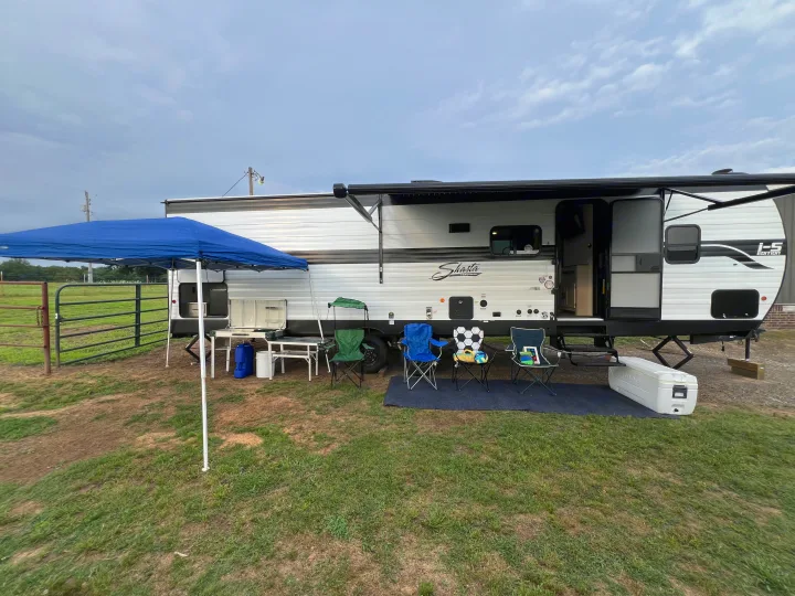 RV rental with outdoor setup: a travel trailer, blue canopy, chairs, and cooler on grass under a cloudy sky.. Forest River Shasta I-5 2026