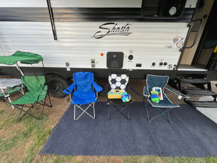 RV rental: Shasta Coachmen trailer with four colorful camping chairs and an outdoor rug on a grassy campsite.. Forest River Shasta I-5 2026