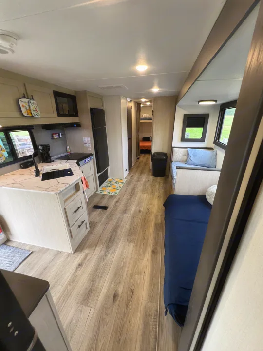 Spacious RV rental interior with a bright kitchen, wood floors, living area with blue seating, and rear bunk beds.. Forest River Shasta I-5 2026