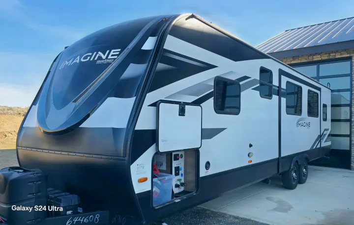 A sleek Imagine Grand Design travel trailer, an ideal rv rental, parked outdoors. Its front utility bay is open, showcasing features.. Grand Design Imagine 2023
