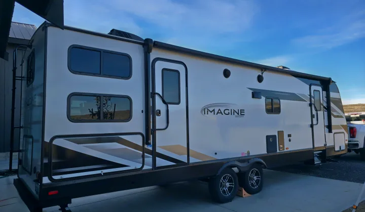 A white Imagine Grand Design travel trailer, ideal for an RV rental, showcasing its side profile, multiple windows, and sleek graphics.. Grand Design Imagine 2023