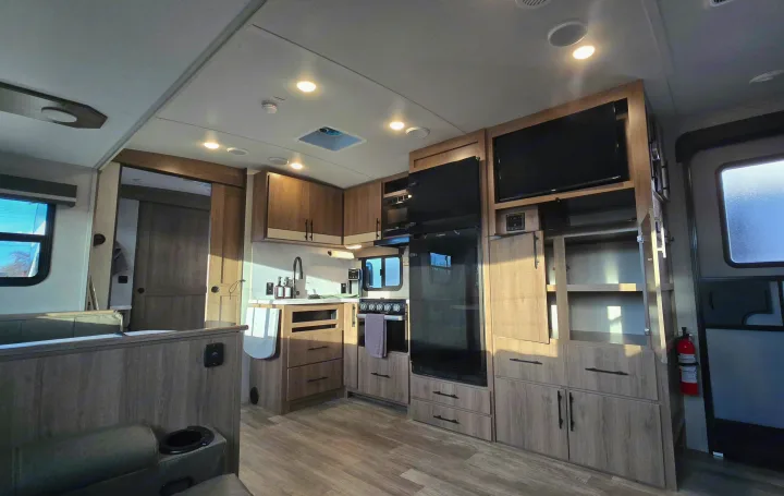 Modern RV rental interior with a spacious kitchen, dining booth, and entertainment setup featuring sleek wood finishes.. Grand Design Imagine 2023