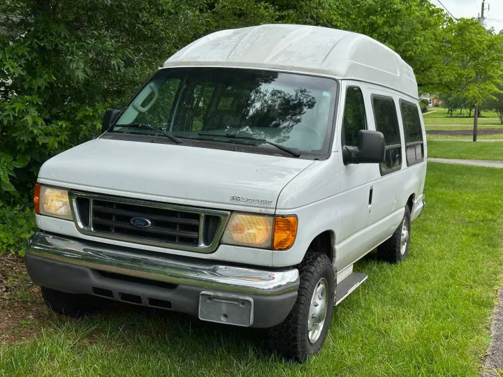 White high-top Ford E-Series conversion van (Transmaster), ideal RV rental, parked on grass by trees on a cloudy day.. Ford E250 Clubwagon 2007