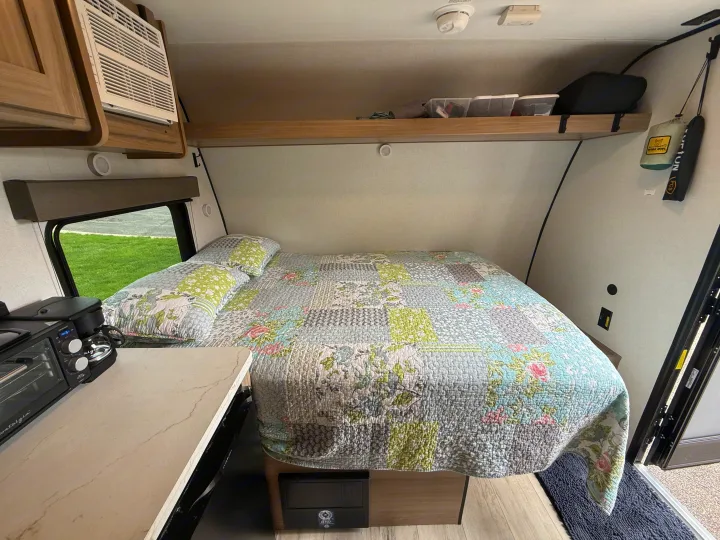Cozy RV rental bedroom with a patchwork quilt, compact appliances, and an AC unit for comfortable travel.. Keystone RV Coleman 13B 2026