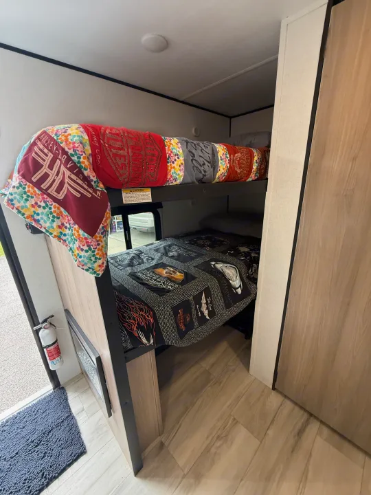 Cozy RV rental interior with bunk beds, Harley-Davidson themed quilts, and a visible fire extinguisher for safety.. Keystone RV Coleman 13B 2026