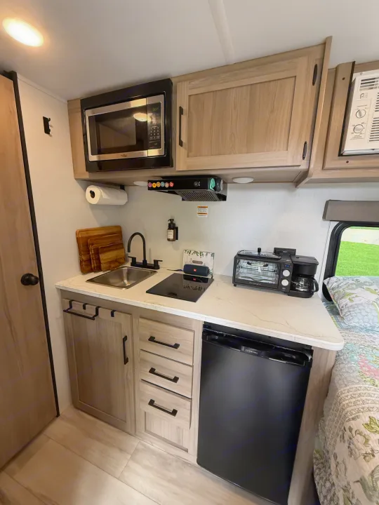 Compact RV rental kitchen features microwave, sink, cooktop, fridge, toaster oven, & coffee maker. Modern design for trips.. Keystone RV Coleman 13B 2026
