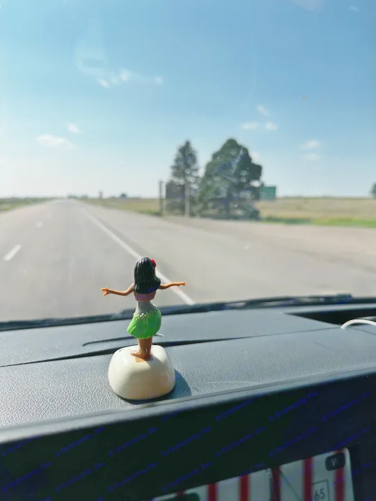 Dashboard hula girl in an rv rental, gazing at the long, empty road under a bright sky. Scenic road trip journey.. Mercedes-Benz Sprinter 2020