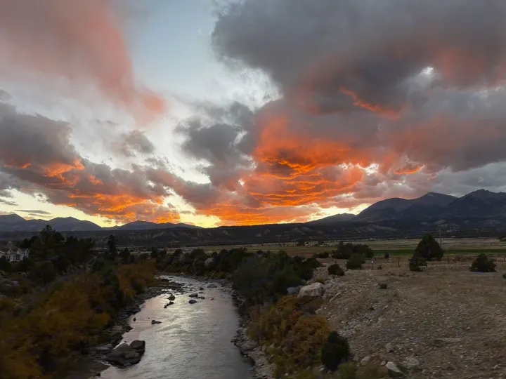 Vibrant orange & grey clouds illuminate a scenic river & mountains at sunset. Perfect for an RV rental adventure!. Mercedes-Benz Sprinter 2020