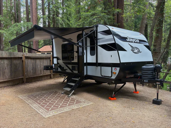 RV rental: White Jayco travel trailer with awning extended at a serene gravel campsite amidst towering redwood trees.. Jayco Jay Feather Air 2025