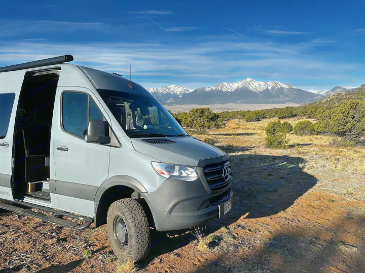 Scenic rv rental: A grey Mercedes Sprinter camper van parked with its door open, facing snow-capped mountains under a blue sky.. Mercedes-Benz Sprinter 2020