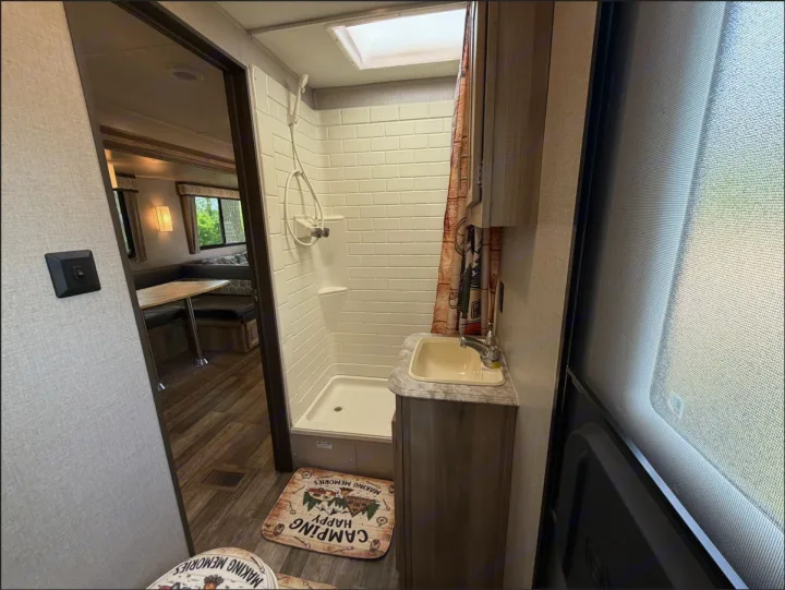 Experience the comfort of an RV rental: a bright bathroom with a tiled shower, sink, and a view into the cozy dinette area.. Coachmen Catalina Legacy 2022