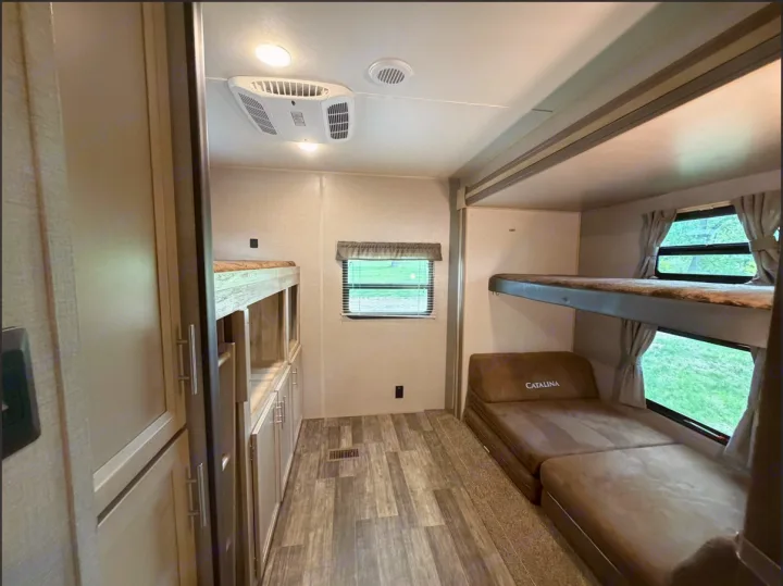 Inside an RV rental bunkhouse: two bunk beds, a convertible sofa, storage cabinets, and windows.. Coachmen Catalina Legacy 2022