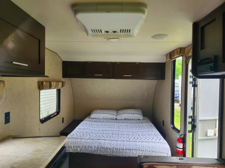 Cozy rv rental bedroom: patterned bed, overhead cabinets, AC unit, window view, and fire extinguisher near the door.. Forest River Cherokee Wolf Pup 2017