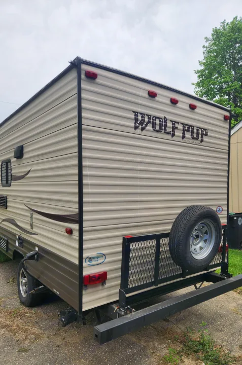 Rear of a beige Wolf Pup travel trailer, shown with spare tire & cargo rack. Available for RV rental from Campers Inn.. Forest River Cherokee Wolf Pup 2017