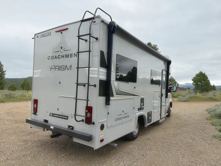 Gray Coachmen Prism RV rental motorhome on gravel. Rear ladder and side awning visible, ready for travel adventures.. Coachmen Prism 2026