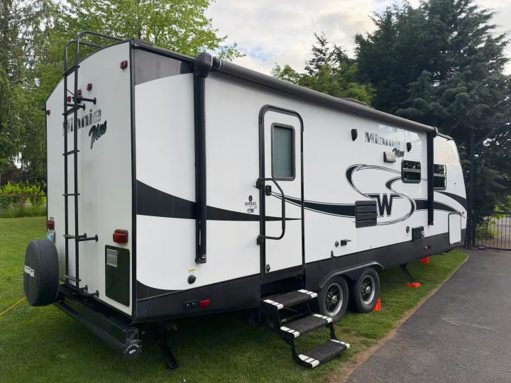 Explore the outdoors with this Minnie Plus RV rental. A white travel trailer, with steps and a rolled awning, is ready for adventure.. Minnie Minnie Plus 2019
