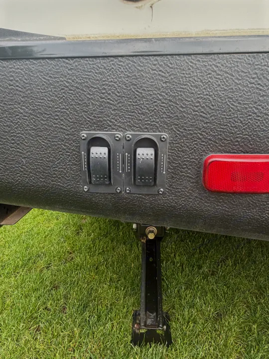 RV rental: textured gray panel with two black 'EXTEND'/'RETRACT' switches for stabilizer jacks, next to a red reflector.. Minnie Minnie Plus 2019