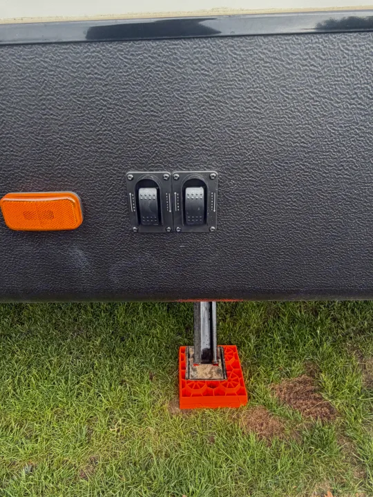 RV rental close-up: stabilizer jack on orange leveling block, with extend/retract controls and orange side reflector.. Minnie Minnie Plus 2019