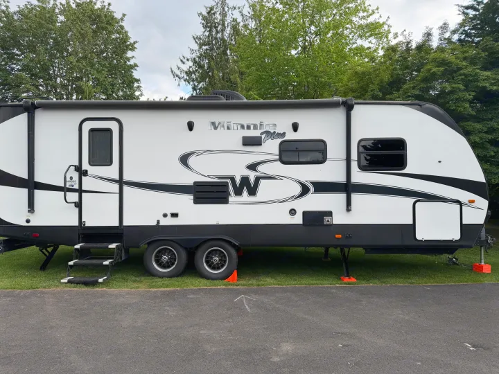 Winnebago Minnie Plus RV rental: a sleek white & black travel trailer parked on grass, surrounded by green trees.. Minnie Minnie Plus 2019