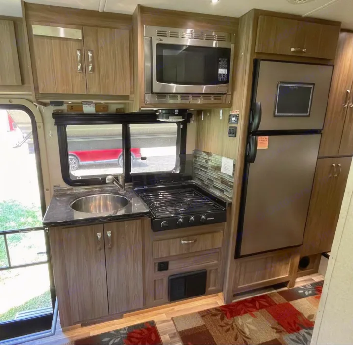 RV rental kitchen view: sink, 3-burner stove, microwave, refrigerator, and wood-tone storage cabinets.. Isata 3 2017