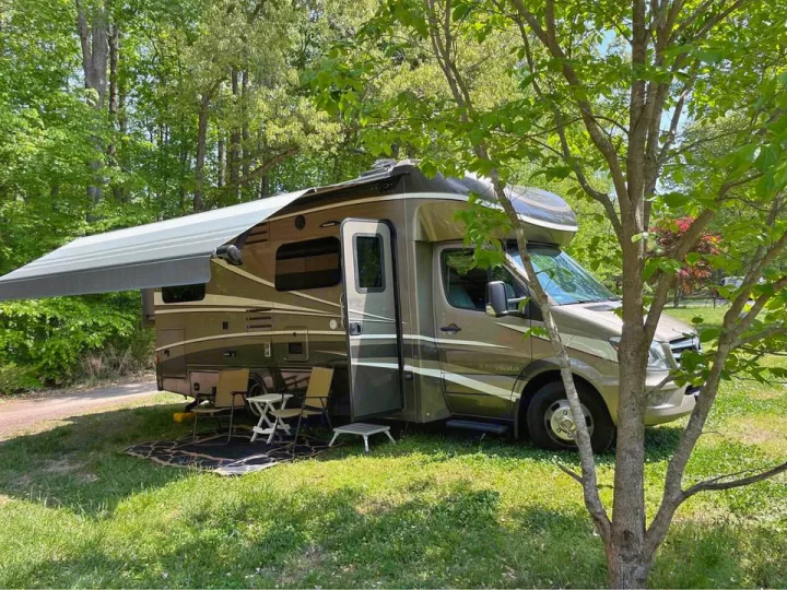 This RV rental motorhome is perfectly set up at a shady campsite with an awning, chairs, and table for outdoor relaxation.. Isata 3 2017