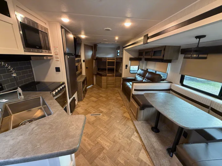 Spacious RV rental interior with a fully equipped kitchen, dining booth, comfy living area, and bunk beds for family comfort.. Forest River Palomino Puma 2022