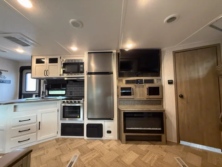 Modern RV rental interior: kitchen with stainless steel appliances, TV, and electric fireplace, light wood-look floor.. Forest River Palomino Puma 2022