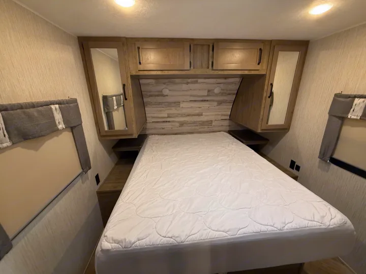 Cozy RV rental bedroom featuring a comfortable bed, built-in overhead cabinets, side shelves, and window blinds.. Forest River Palomino Puma 2022