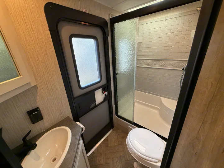 RV rental bathroom interior with sink, toilet, and shower. Features a door with an 'EXIT' sign, modern fixtures, and wood-look finishes.. Forest River Palomino Puma 2022