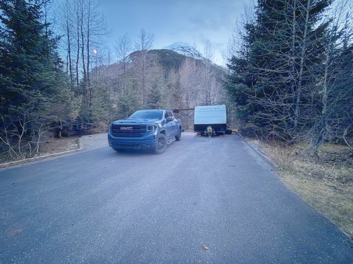 Blue GMC truck with a Prowler travel trailer RV rental at a mountain campsite under a moonlit, twilight sky.. Heartland RVs Prowler Lynx 2024