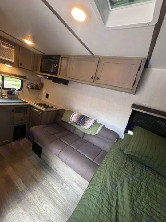 Inside a modern RV rental: a compact kitchen, comfortable gray sofa, and green bed. Enjoy practical camper living.. Sunset Park RV Sun Lite LTD 13MJ 2025