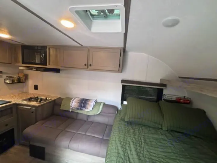 Cozy RV rental interior featuring a compact kitchen, L-shaped seating area, and a bed with green bedding.. Sunset Park RV Sun Lite LTD 13MJ 2025