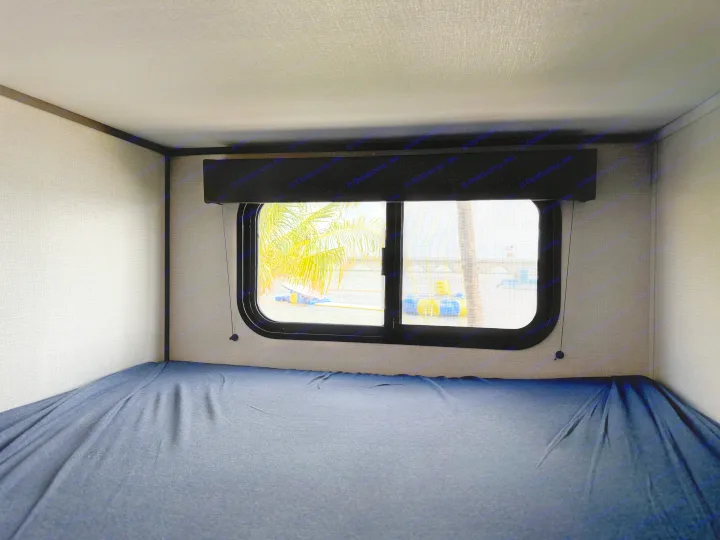 Inside an RV rental: a bunk bed with blue sheets and a window revealing palm trees, water, and a bridge.. Grand Design Transcend Xplor 2026