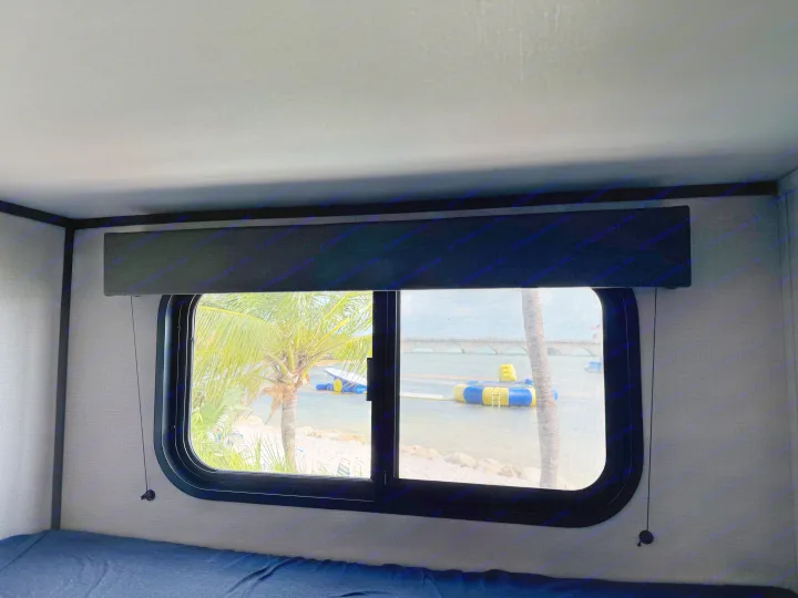 Tropical paradise view from an RV rental, showing palm trees, sandy shore, water toys, and a bridge in the distance.. Grand Design Transcend Xplor 2026
