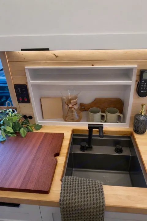 Modern RV rental kitchen featuring a pour-over coffee station, black sink, wood countertops, and neat storage for essentials.. Ford Transit 2023