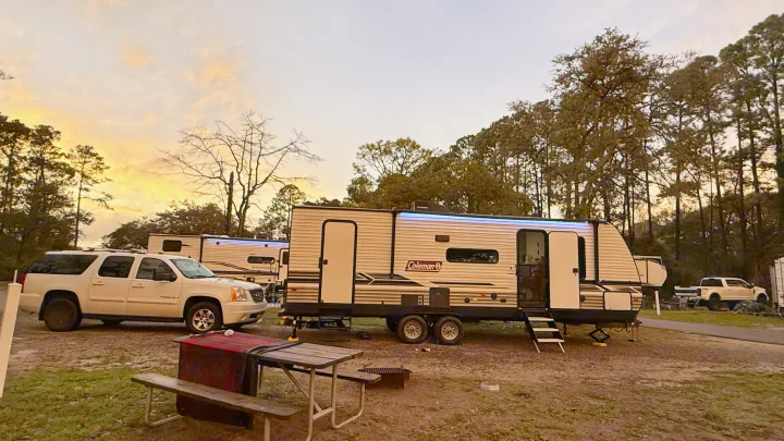 A Coleman RV rental is parked at a scenic campsite with an SUV, picnic table, and trees under a sunset sky.. Dutchmen Coleman Lantern LT 2024
