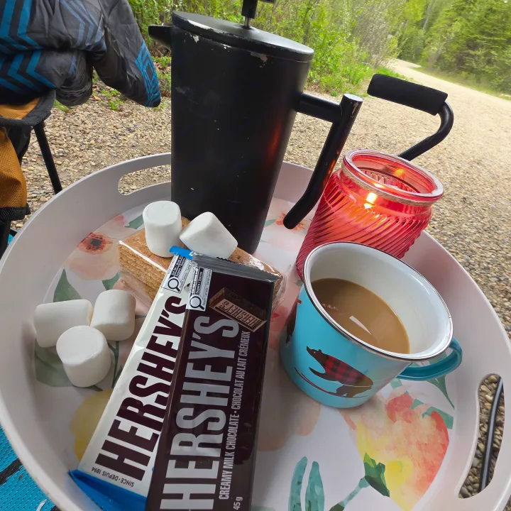 Enjoying s'mores ingredients & coffee from an RV rental. A French press, chocolate, marshmallows, and candle on a tray outdoors.. Outdoors RV 23DBS 2023