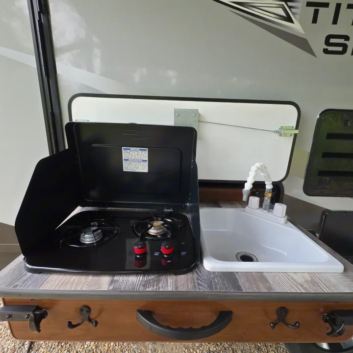This RV rental features a convenient pull-out outdoor kitchen with a two-burner camping stove and a compact sink, perfect for roadside cooking.. Outdoors RV 23DBS 2023