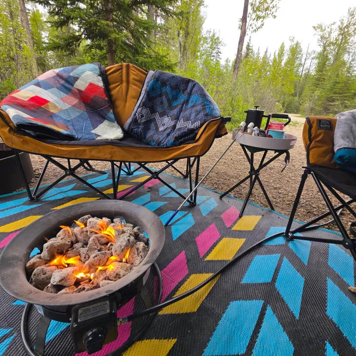 Relaxing RV rental camping setup: propane fire pit, cozy chairs with blankets, and a side table for s'mores in nature.. Outdoors RV 23DBS 2023