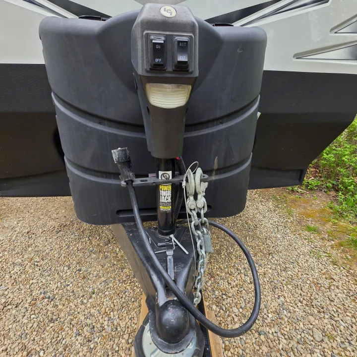 Front hitch, power tongue jack, and propane tank cover of an RV rental on gravel. Essential for coupling a travel trailer.. Outdoors RV 23DBS 2023