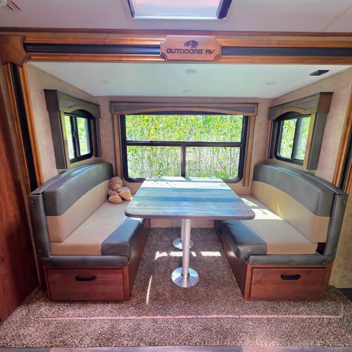Enjoy meals in this comfortable RV rental dinette featuring booth seating, a sturdy table, and large windows with outdoor views.. Outdoors RV 23DBS 2023