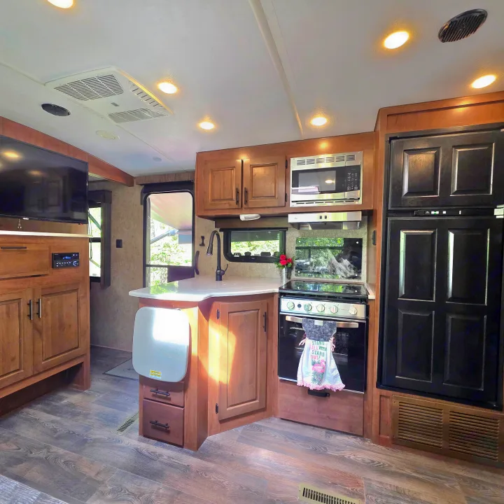 Spacious RV rental kitchen features modern appliances, wood cabinets, TV, and light-colored counters for comfortable travel.. Outdoors RV 23DBS 2023