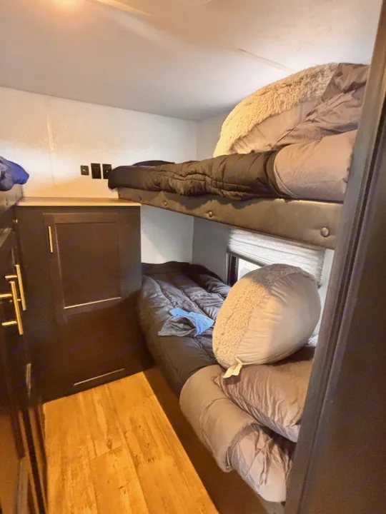 Cozy RV rental bunk beds with dark bedding, cabinets, and wood flooring, perfect for comfortable family travel.. Forest River Cherokee Grey Wolf 2021