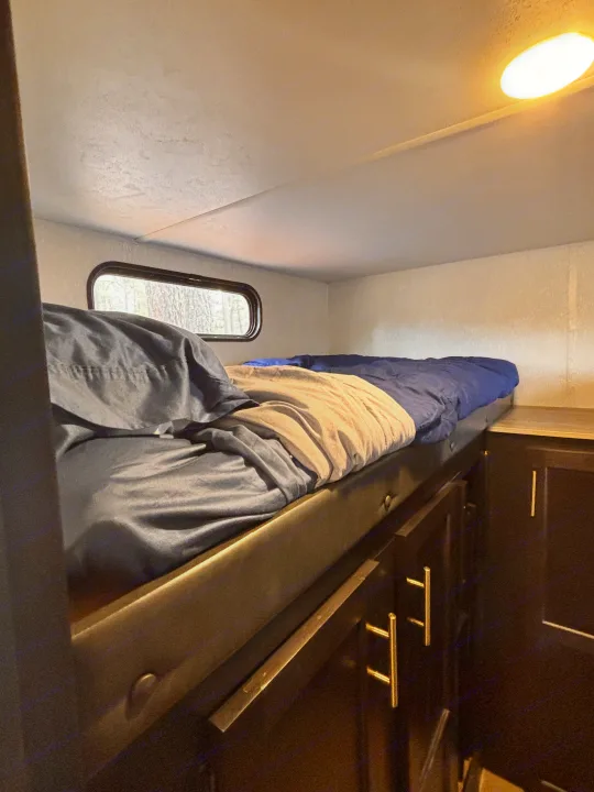 This RV rental features a cozy bunk bed with blue bedding, a window view, and dark storage cabinets below for camping.. Forest River Cherokee Grey Wolf 2021