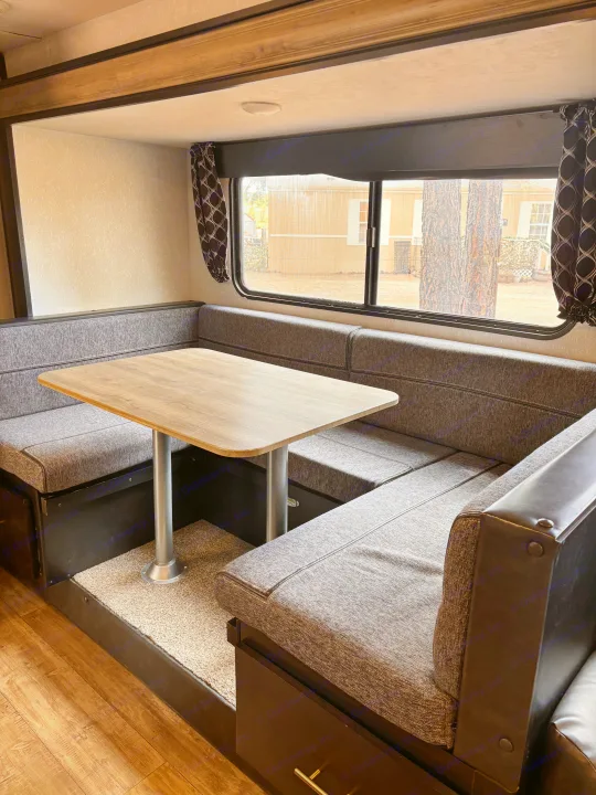 This inviting RV rental dinette features U-shaped grey seating, a wooden table, and a window view, perfect for meals and relaxation.. Forest River Cherokee Grey Wolf 2021
