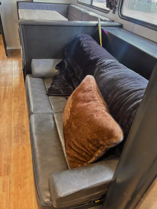 Interior view of an RV rental: comfy gray sofa with a fur pillow, blanket, and dining booth.. Forest River Cherokee Grey Wolf 2021